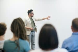 Mann hält Vortrag vor einem Publikum mit weißem Hintergrund.