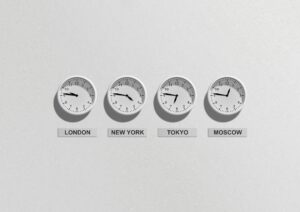 Vier weiße Uhren nebeneinander an einer weißen Wand. Die Uhren zeigen die Zeit an in London, New York, Tokio, Moskau.