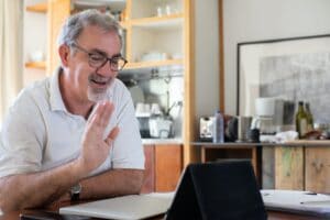 Älterer Mann sitzt vor dem Laptop und spricht online mit Personen