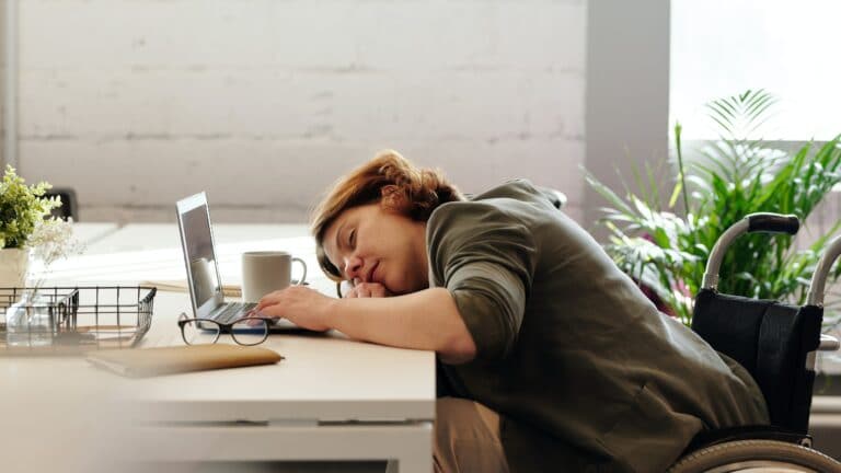 Eine Frau schläft vor einem Laptop mit der Hand auf der Tastatur und dem Kopf auf einem Arm abgelegt.
